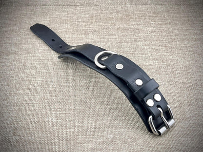 Black leather cuff with silver hardware on a textured beige background