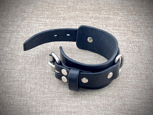 Black leather cuff with silver studs on a textured gray background