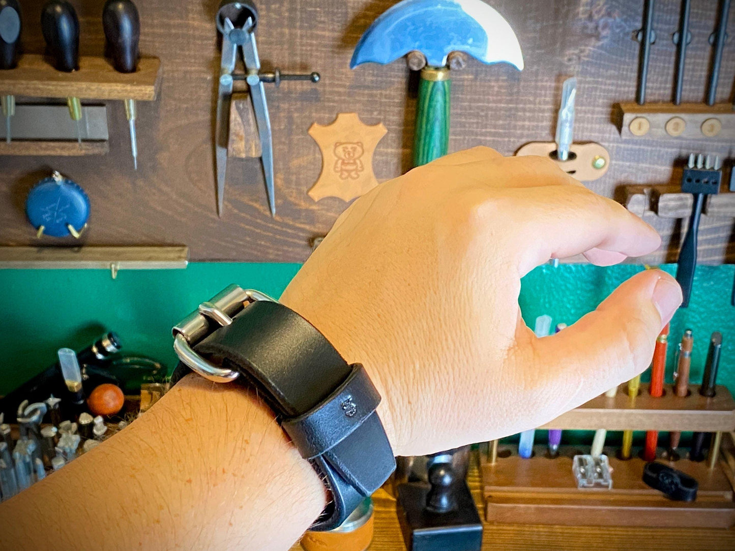 Hand wearing a black leather watch with tools and equipment in the background