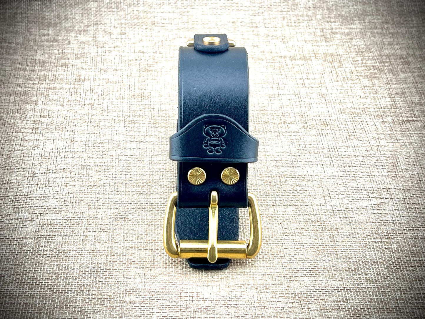 Black leather wristband with gold buckle on a textured gray background