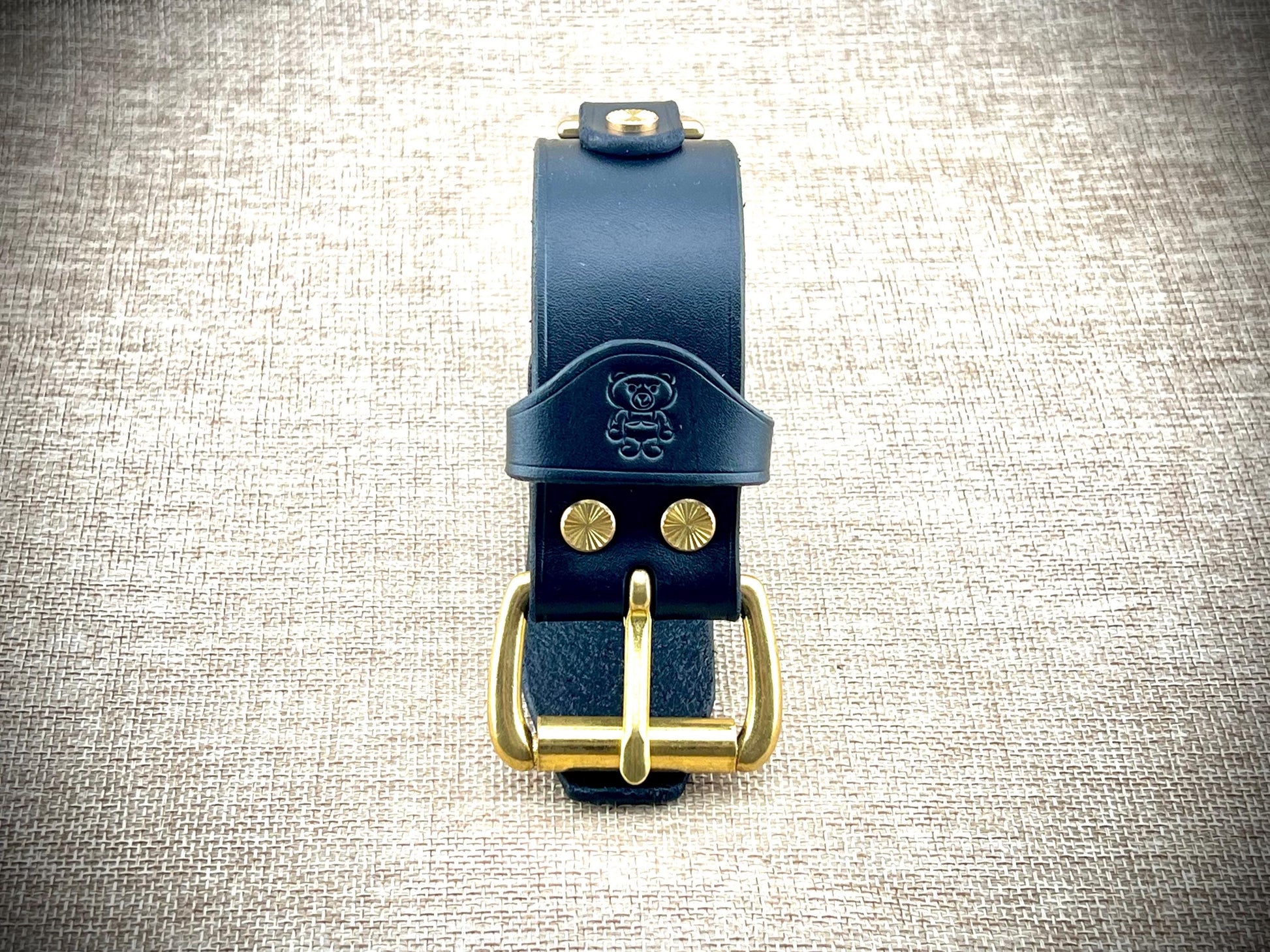 Black leather wristband with gold buckle on a textured gray background