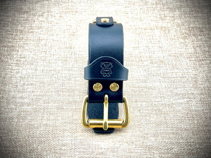 Black leather wristband with gold buckle on a textured gray background