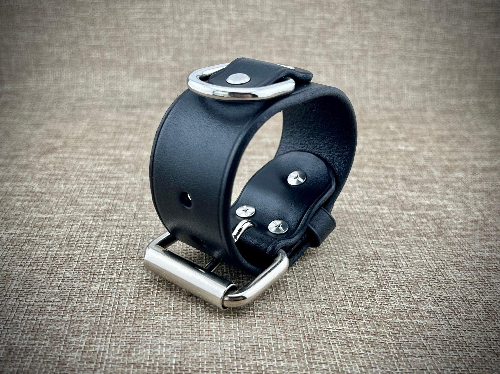 Black leather wristband with silver hardware on a textured brown background