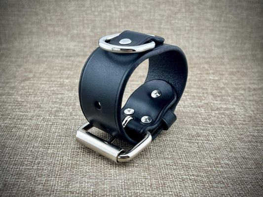 Black leather wristband with silver hardware on a textured brown background